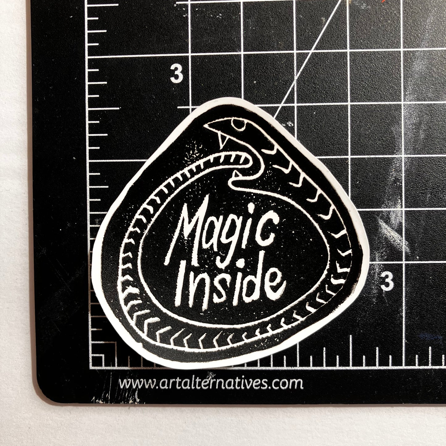 Black and white sticker with 'Magic Inside' text on a cutting mat.