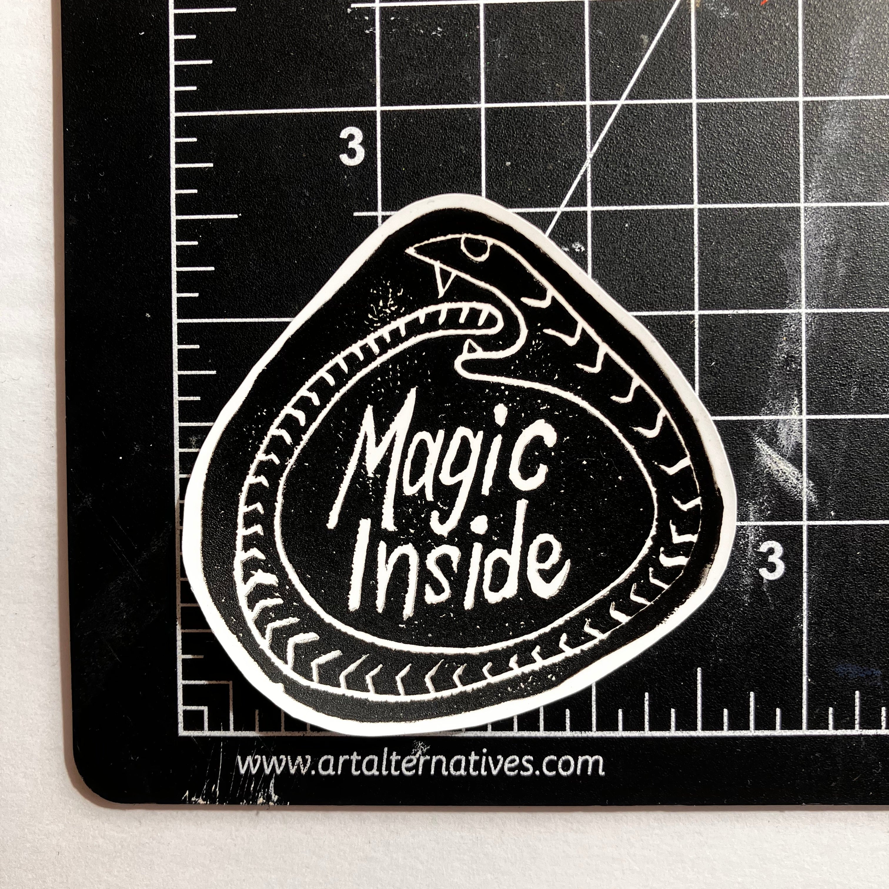 Black and white sticker with 'Magic Inside' text on a cutting mat.